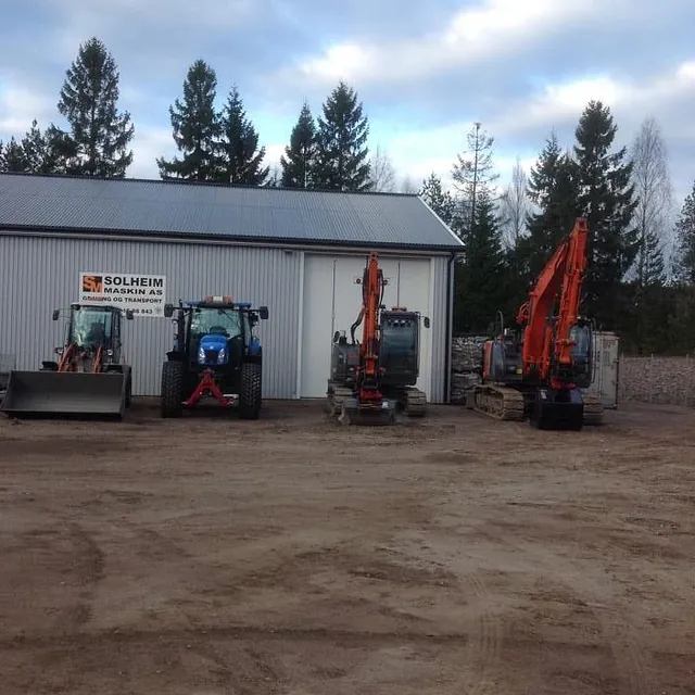 Maskiner parkert foran en hvit hall med skiltet "Solheim Maskin AS".