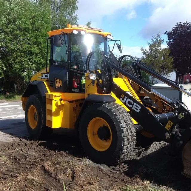 En gul JCB hjullaster står parkert på en jordet overflate med grønt landskap bak.